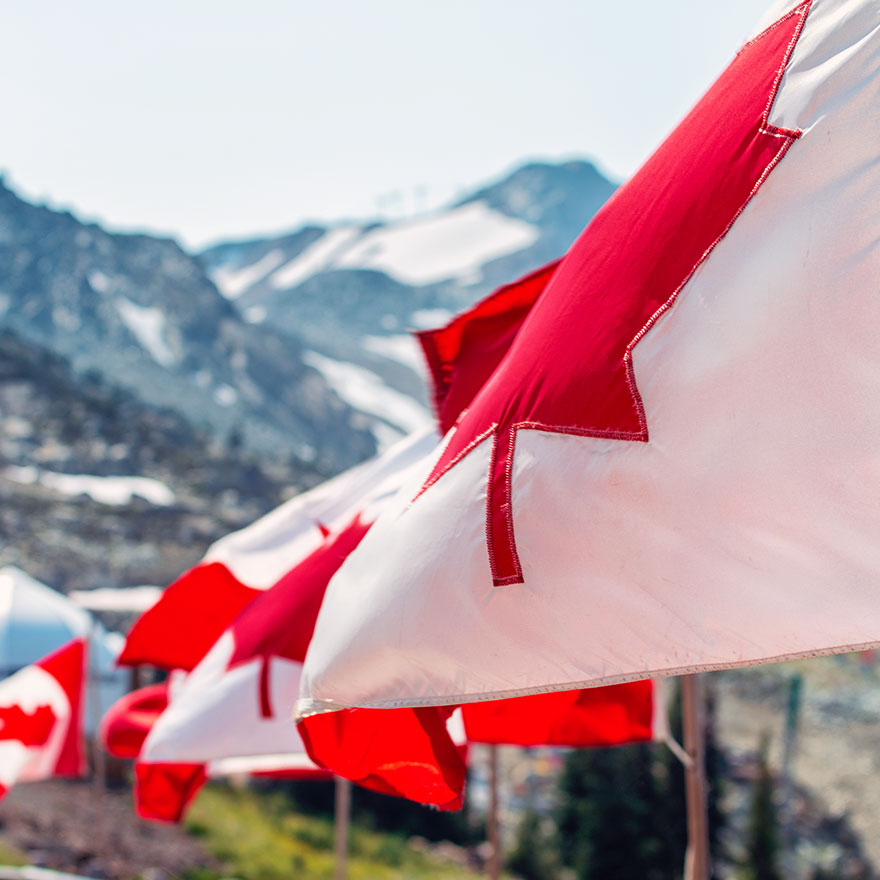 Canadian Flags blowing in the wind with mountains in the background.